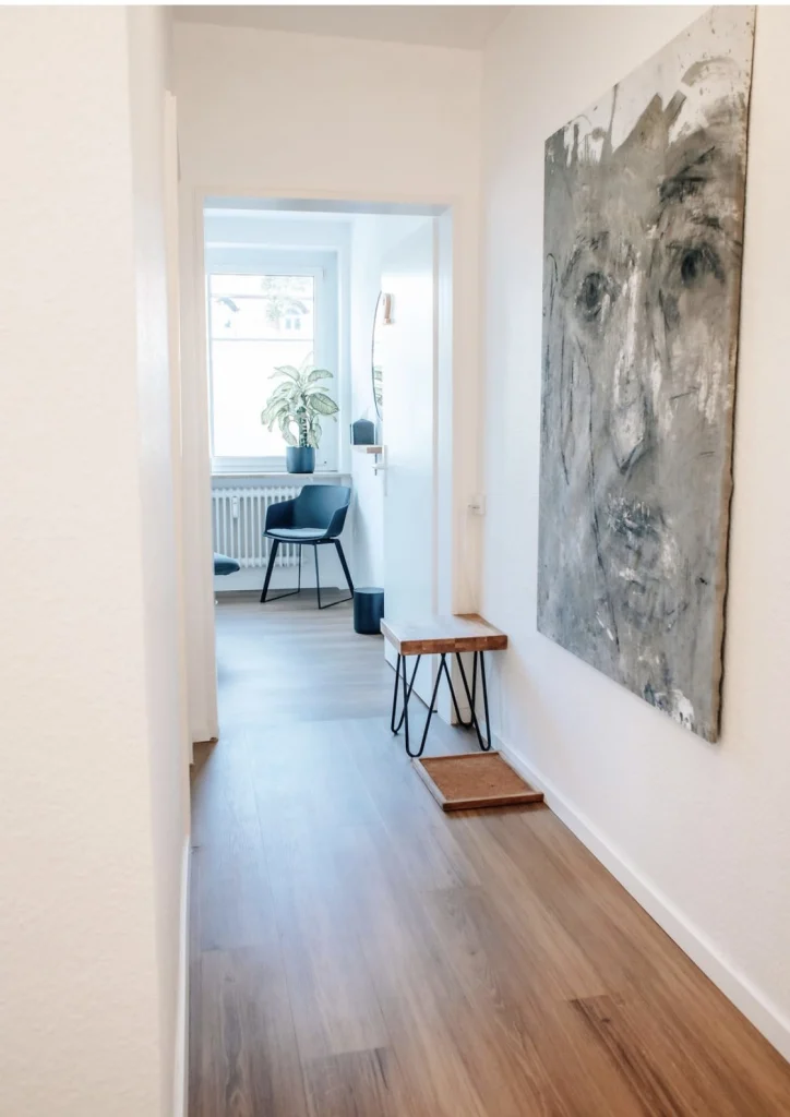 Schmaler Praxisflur mit großem Gemälde, Hocker und Blick in einen Behandlungsraum